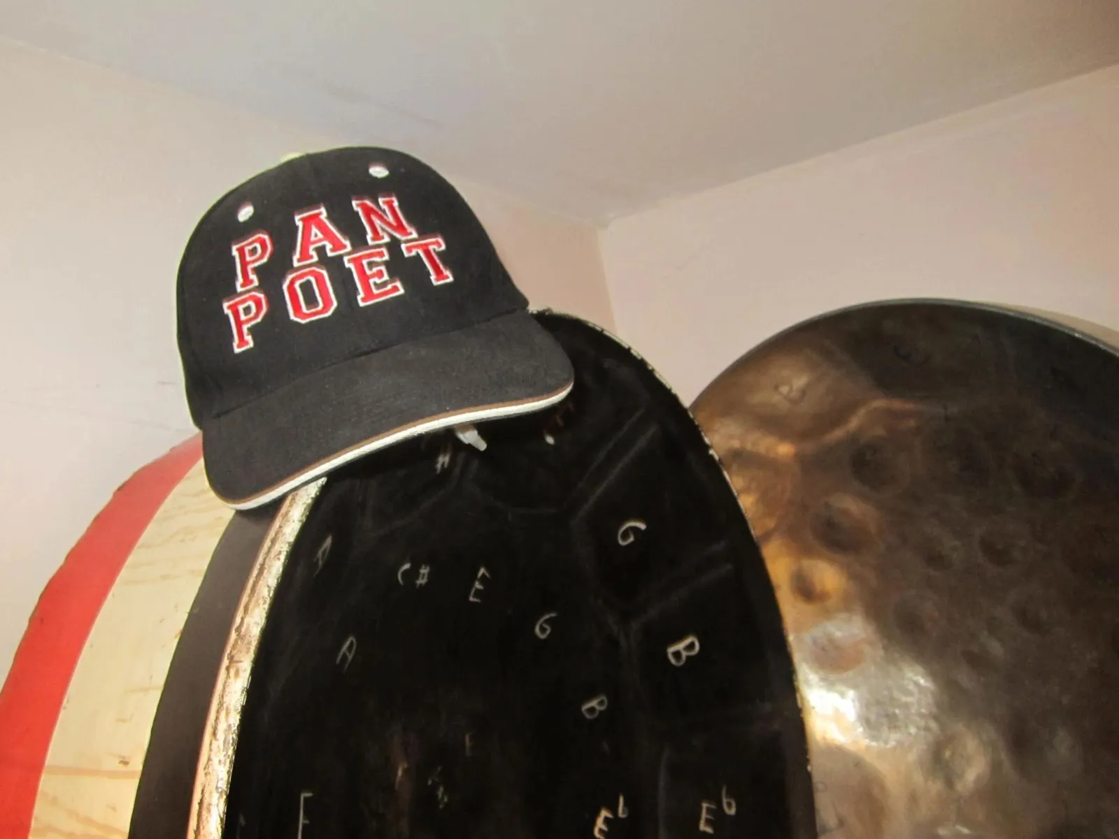 Black cap reading PAN POET resting on a steelpan